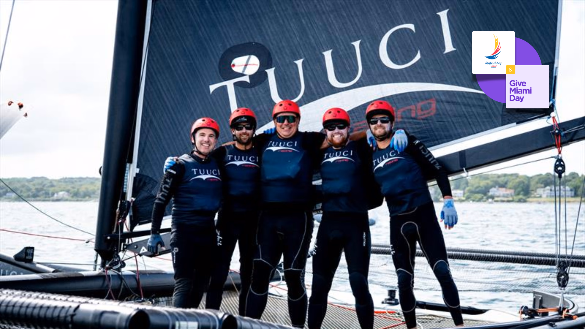 An M32 racing team in matching gear standing in front of their catamaran