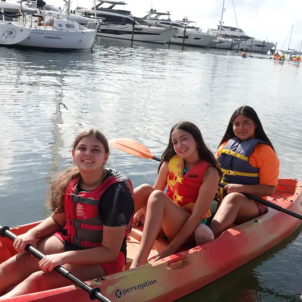 Three young sailors in life vests paddling a kayak together in shallow water