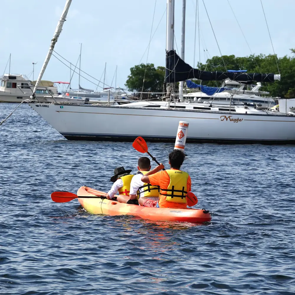Paddlers in a kayak passing the sailboats moored off the dock