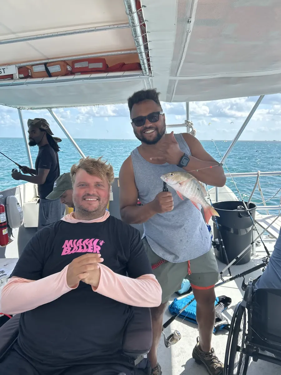 A participant holding up the fish he just landed, with a volunteer and a dog aboard the boat