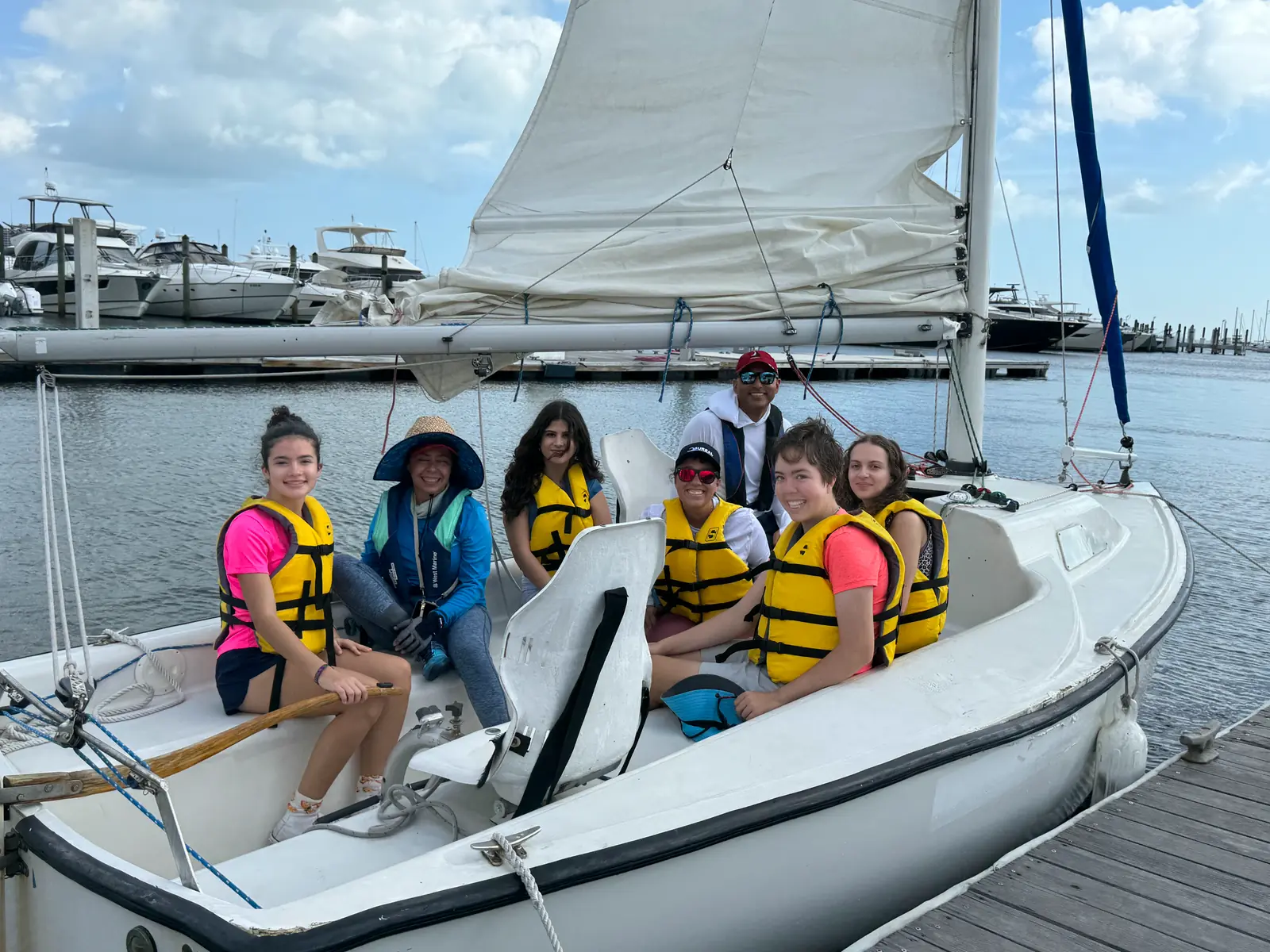 Campers in life vests seated around the cockpit of a sailboat