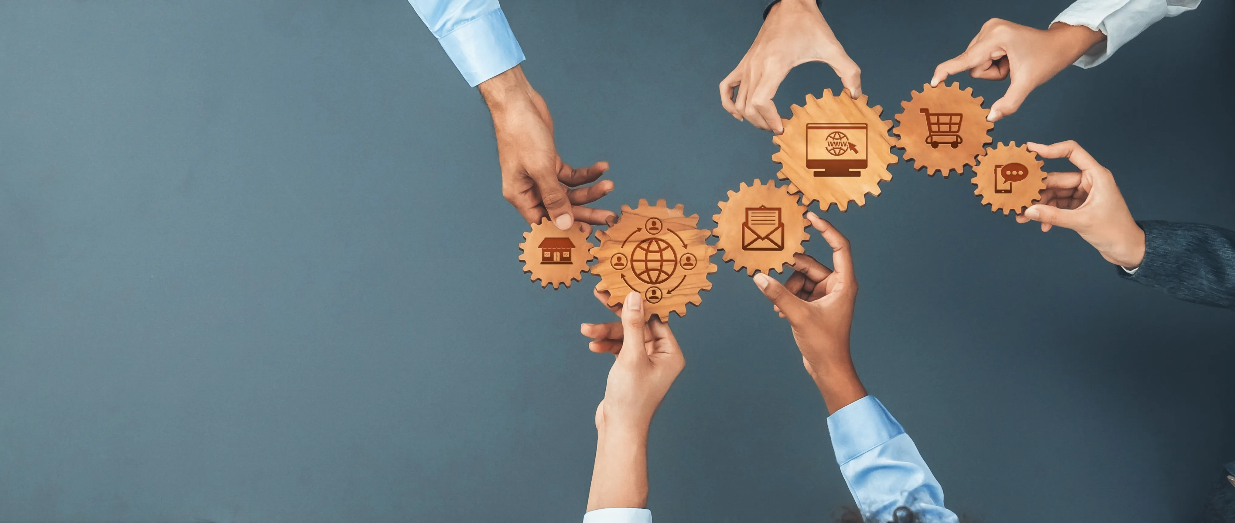Team hands linking wooden gears marked with store, email, website, shopping cart, and mobile chat icons around a global network