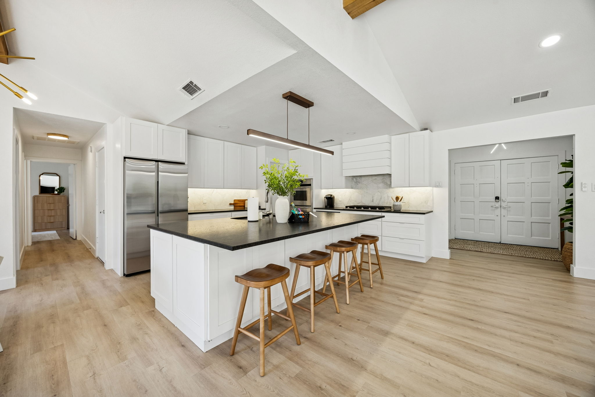 White kitchen with a waterfall island, four blue-grey stools and a round dining table.