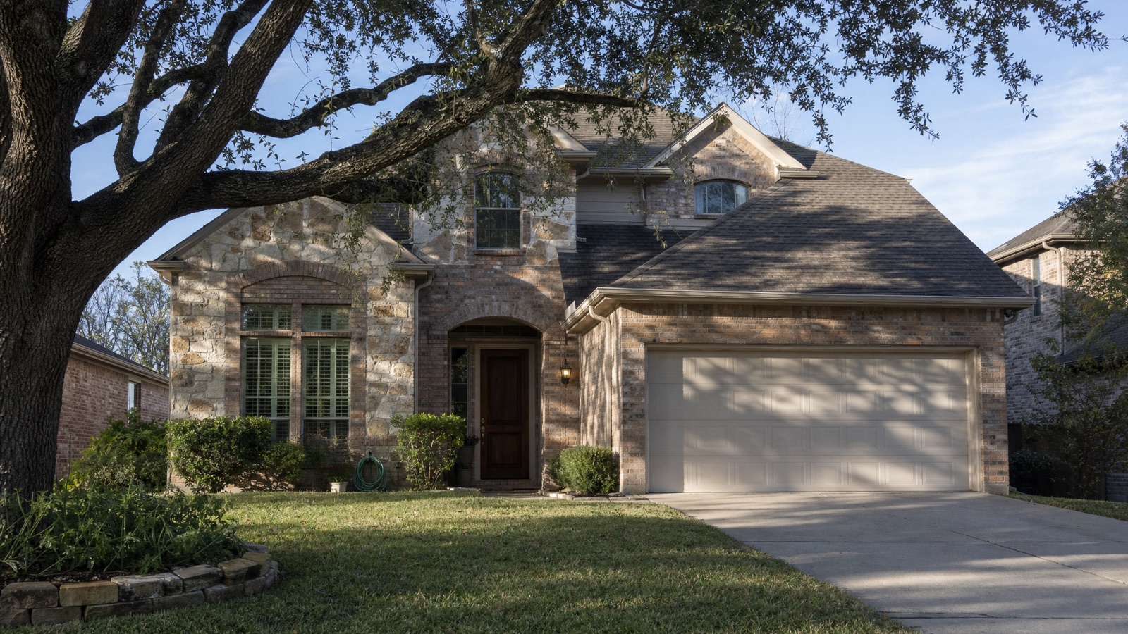 Brick and stone single-family home under a live oak in a Texas suburb