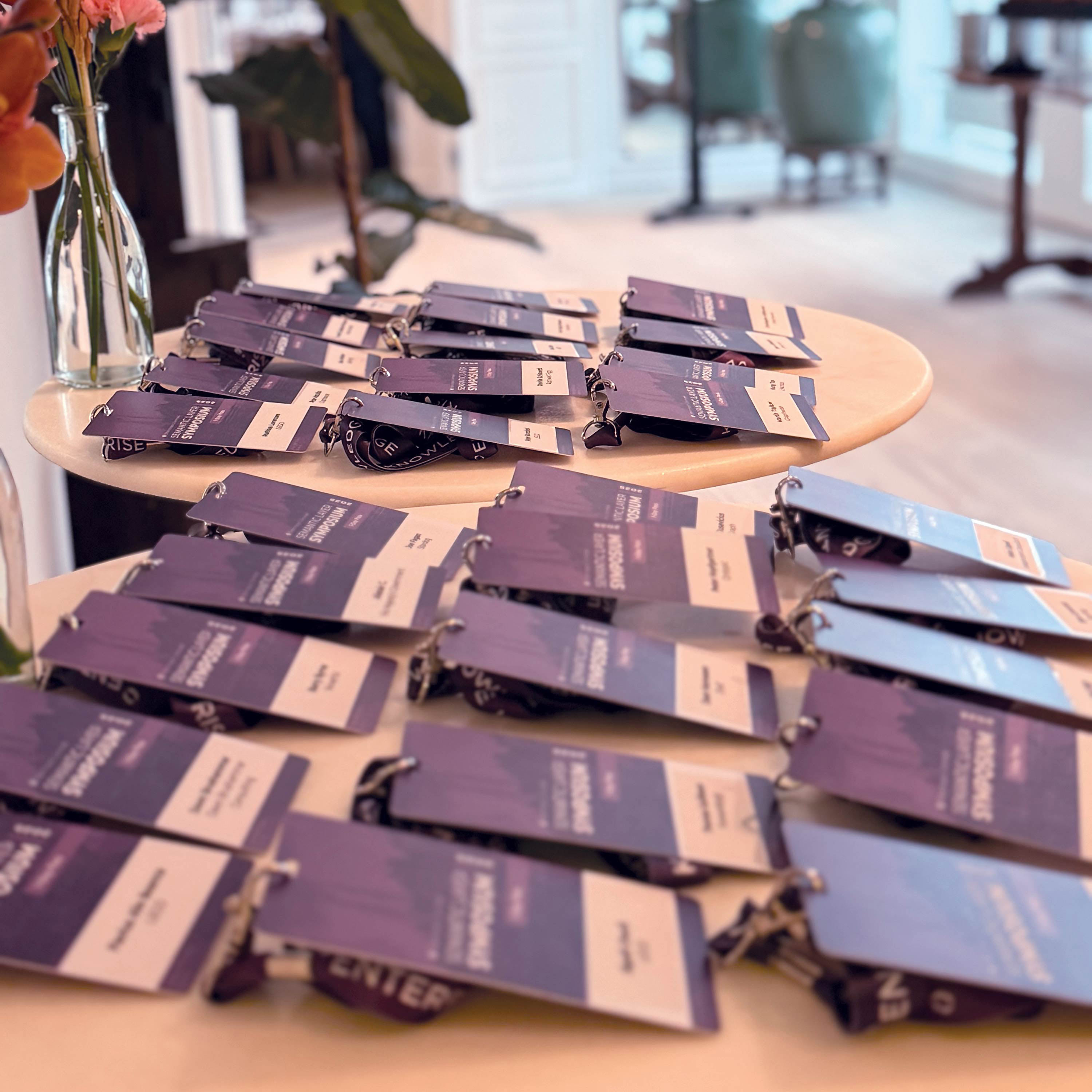 Purple and white event lanyards with badges arranged on round tables in a bright room.