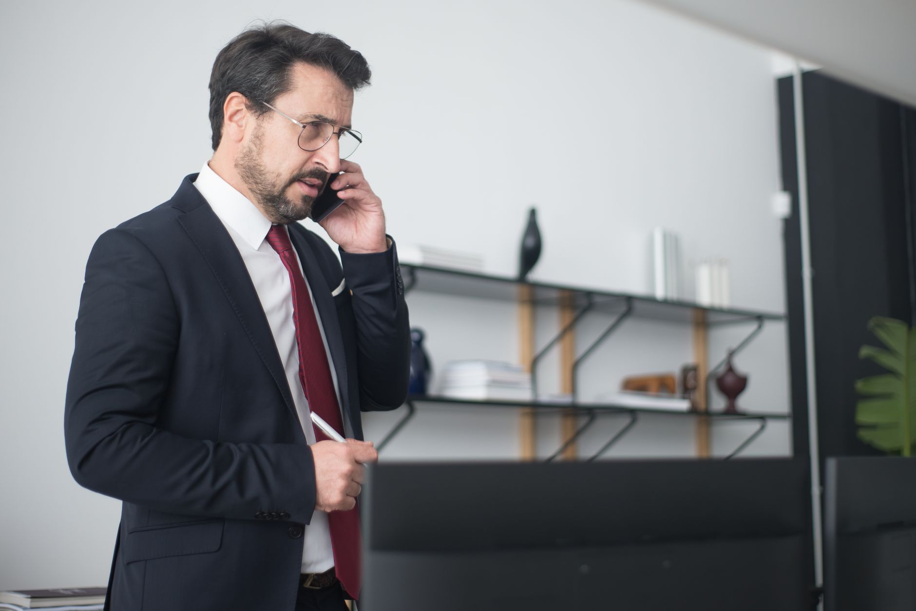 Businessman in a suit taking a mobile phone call in a modern office, illustrating AI voice clone fraud targeting bank executives