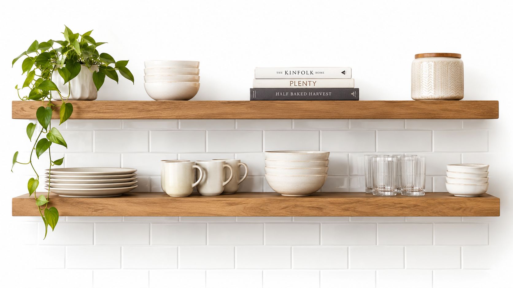 Two wooden floating shelves mounted on a white subway tile wall featuring organized kitchenware and plants.