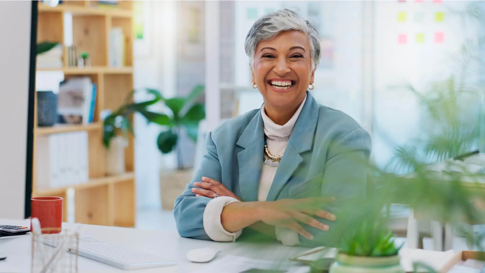 Smiling professional woman in a modern office environment with natural light and plants, exuding confidence and positivity.