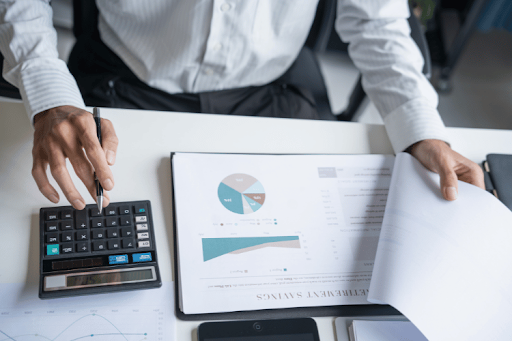 Business professional reviewing financial reports and calculating marketing performance metrics using analytics data and a calculator