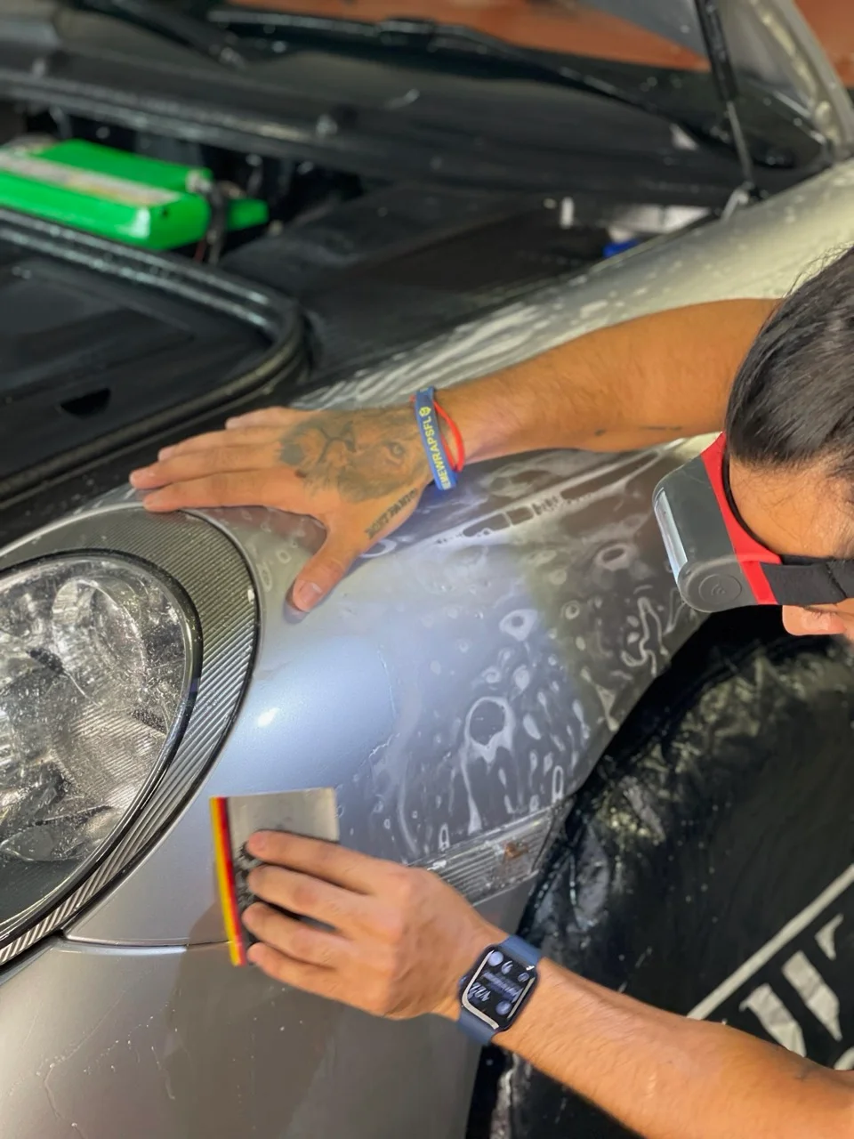 Detailer installing paint protection film on the front fender and headlight of a silver Porsche at Allure Auto Spa in Casselberry, Florida.