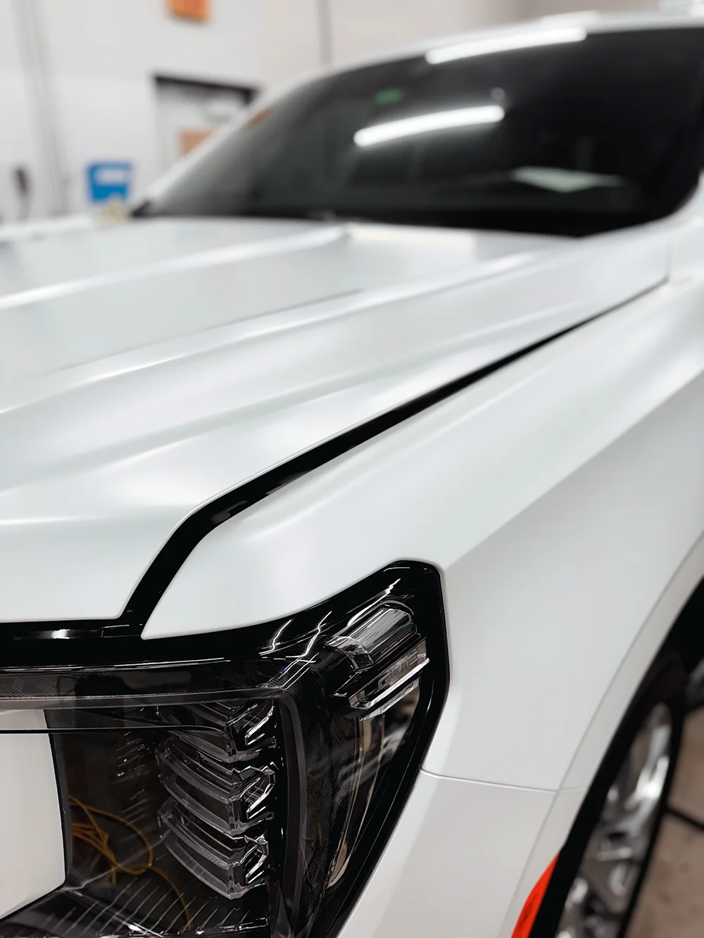 Close-up of white wrapped GMC Sierra hood with black headlight trim at Allure Auto Spa in Casselberry, Florida