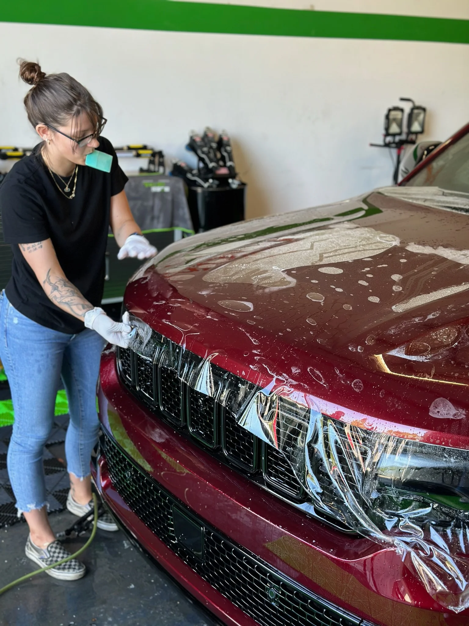 Technician applying paint protection film to the front of a maroon Jeep Grand Cherokee at Allure Auto Spa in Casselberry, Florida