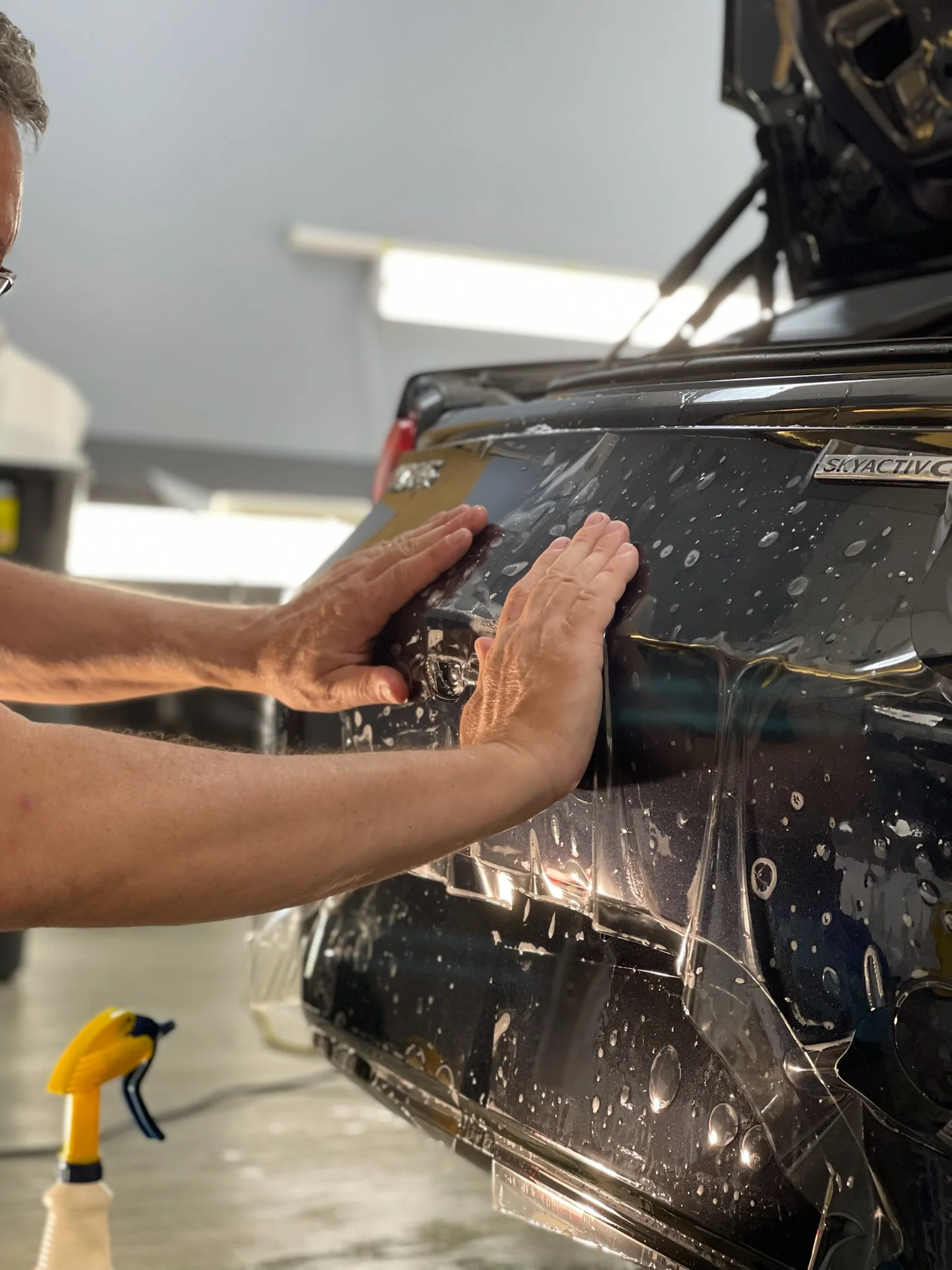 Close-up of technician applying paint protection film to the rear bumper of a black Mazda CX-5 at Allure Auto Spa in Casselberry, Florida