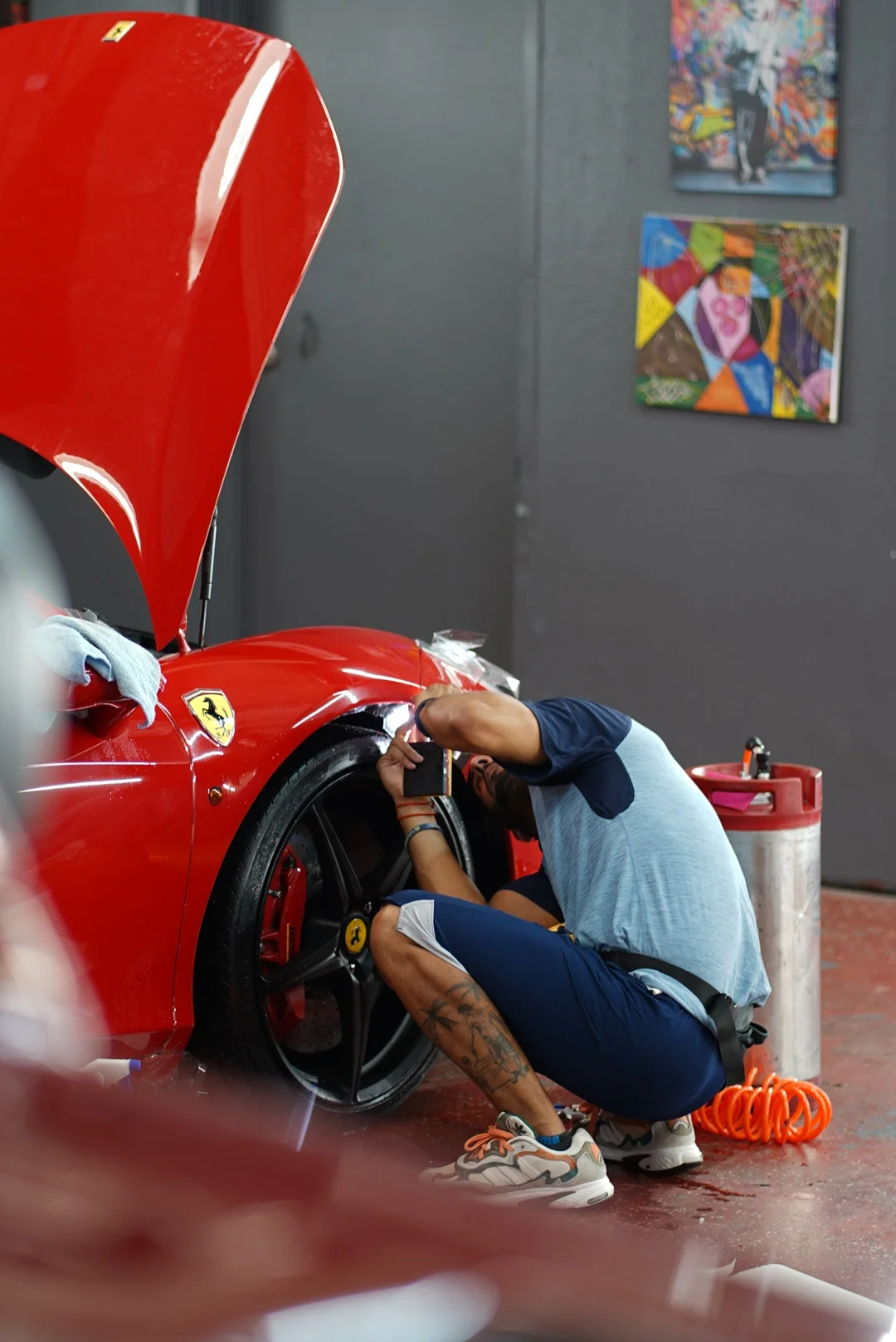 Close-up of technician installing paint protection film on the wheel arch of a red Ferrari 488 at Allure Auto Spa in Casselberry, Florida