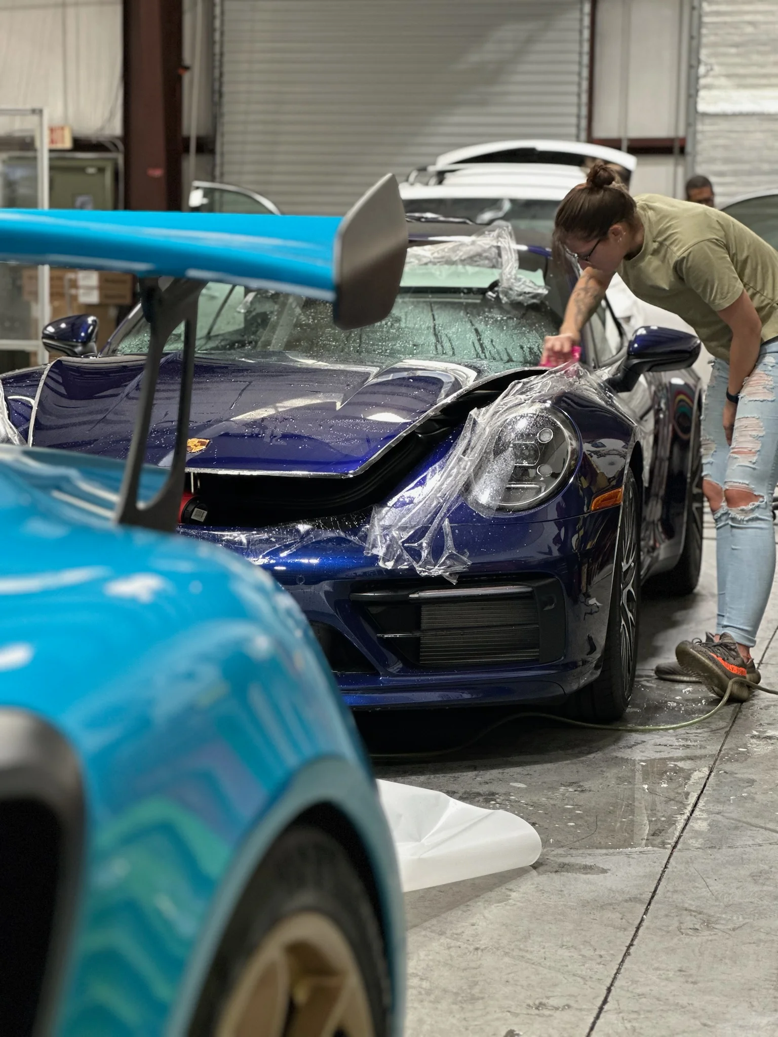 Technician applying paint protection film to a blue Porsche 911 GT3 at Allure Auto Spa in Casselberry, Florida
