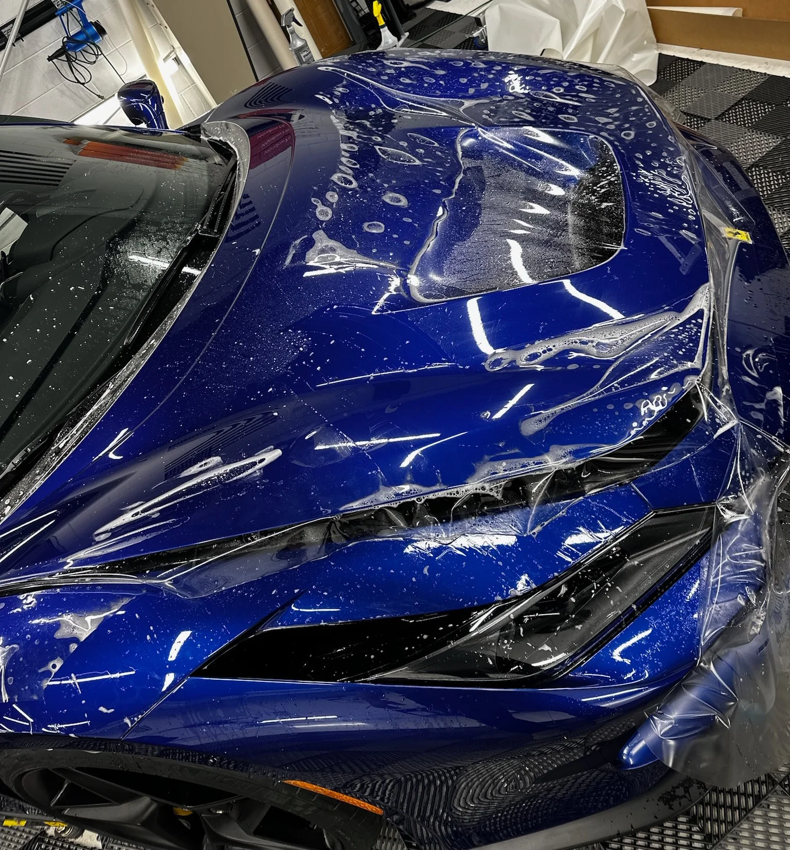 Close-up of paint protection film being applied to the hood of a blue Ferrari at Allure Auto Spa in Casselberry, Florida