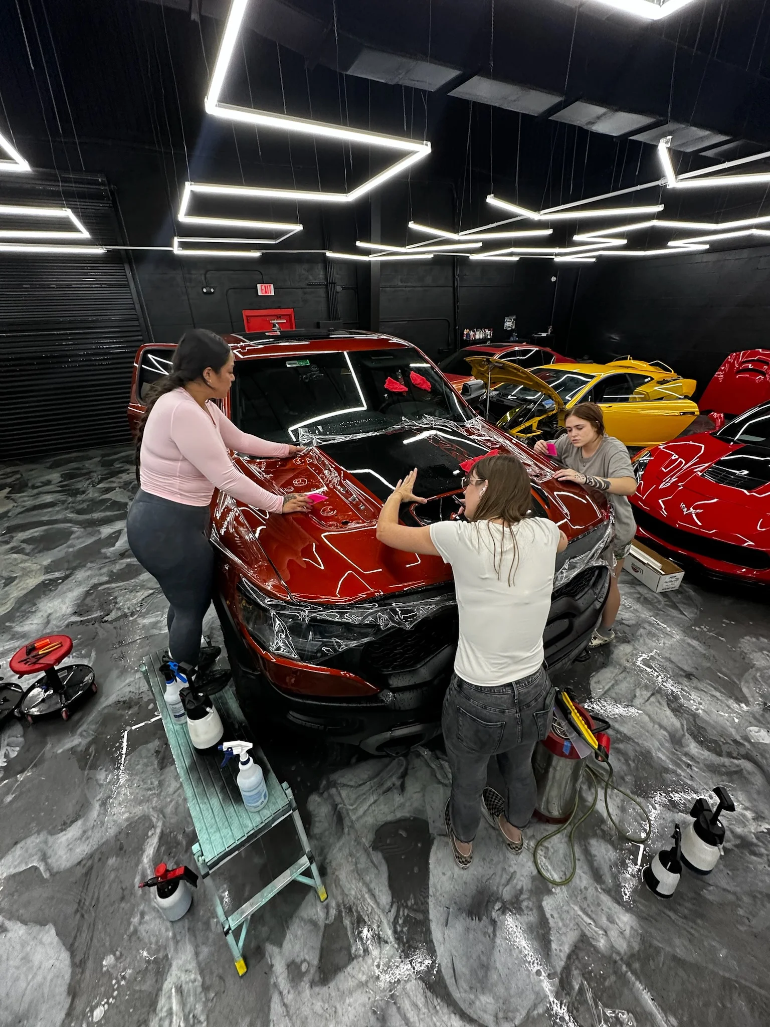 Three technicians working together to apply paint protection film on the hood of a red RAM TRX at Allure Auto Spa in Casselberry, Florida