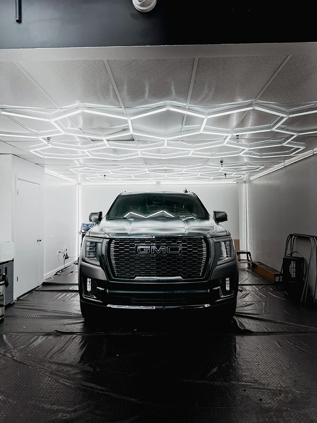 Front view of a large GMC Yukon SUV with a custom dark grey car wrap, parked under accent lighting at Allure Auto Spa