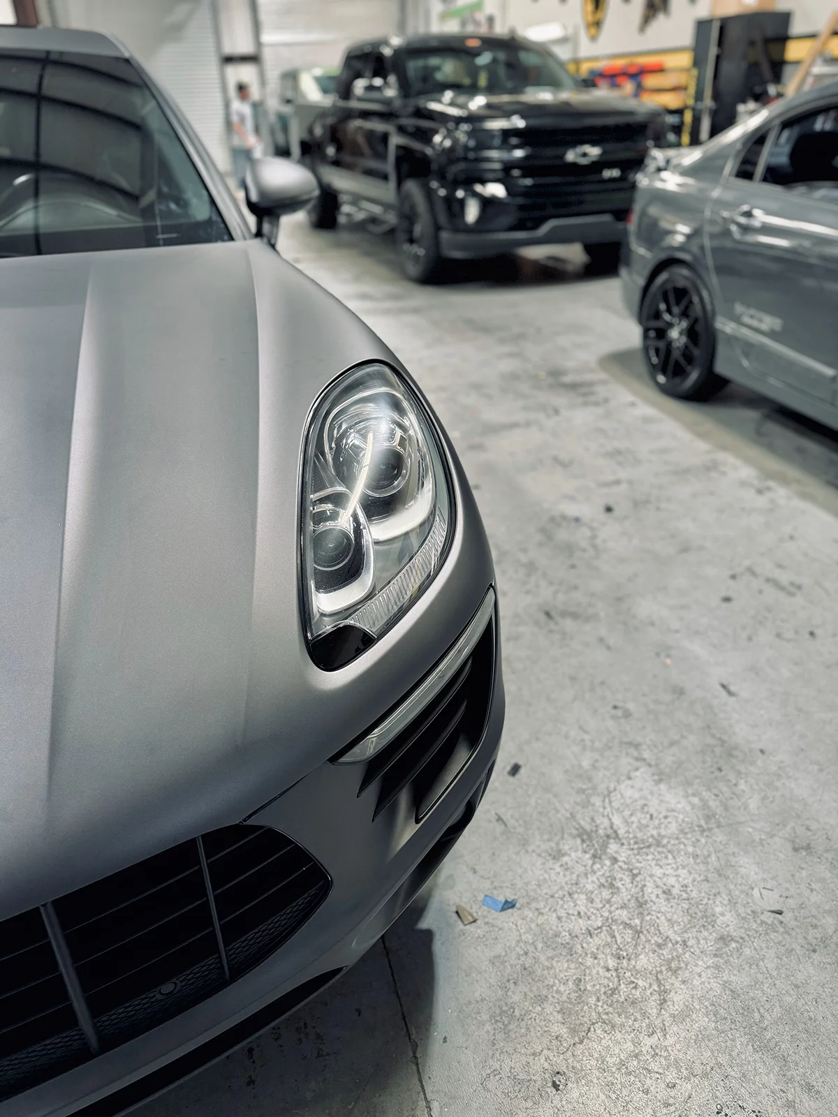 Close-up of a Porsche Macan with a refined satin grey car wrap, highlighting the headlight and grille detail by Allure Auto Spa