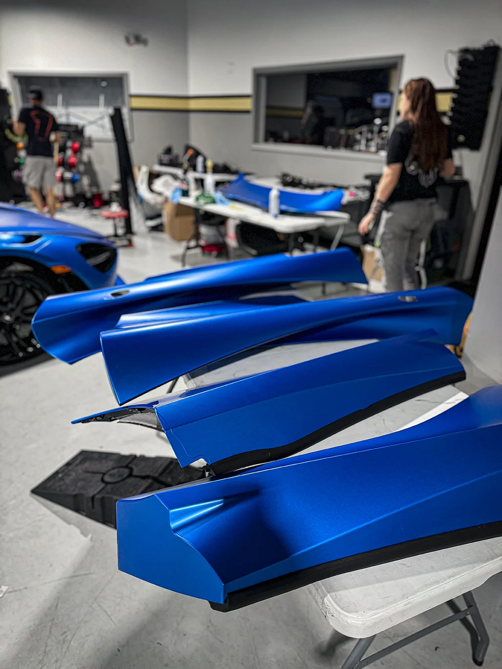 Custom satin blue wrapped body panels of a McLaren 720S laid out during the vehicle wrap process at Allure Auto Spa