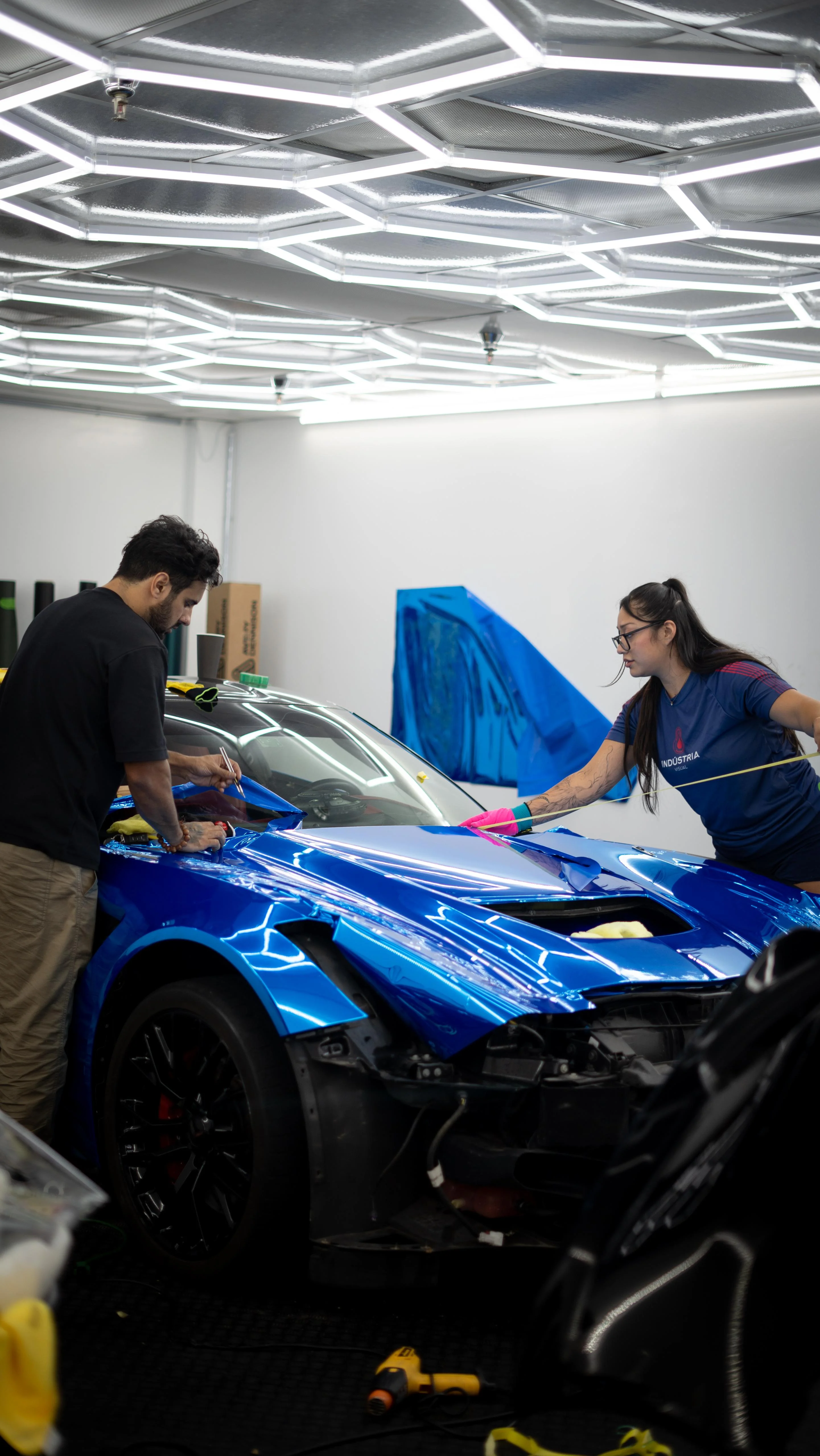 Allure Auto Spa team members collaborating on a vibrant blue car wrap installation for a Chevrolet Corvette C7