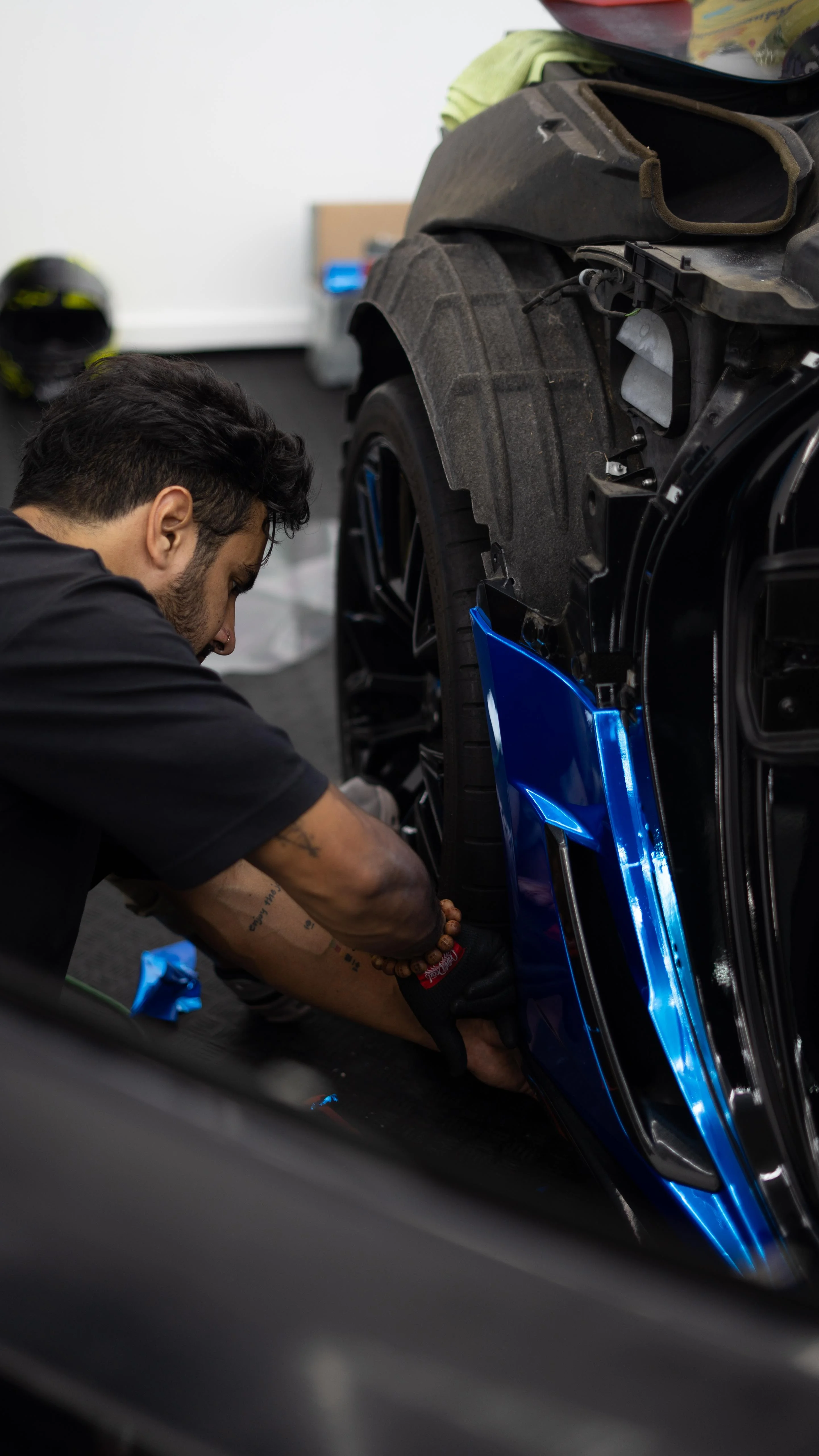 A technician from Allure Auto Spa installing a bright blue car wrap on the fender of a Chevrolet Corvette C7