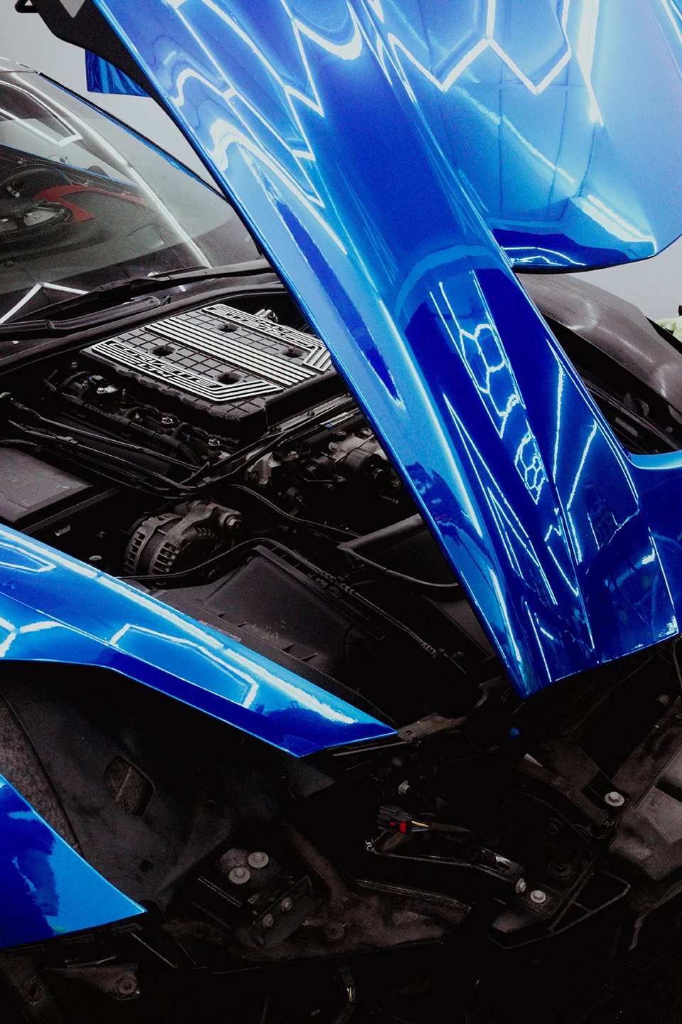 Close-up detail of a stunning blue metallic car wrap on the hood of a Chevrolet Corvette C7 Z06, reflecting the hexagonal shop lights, at Allure Auto Spa