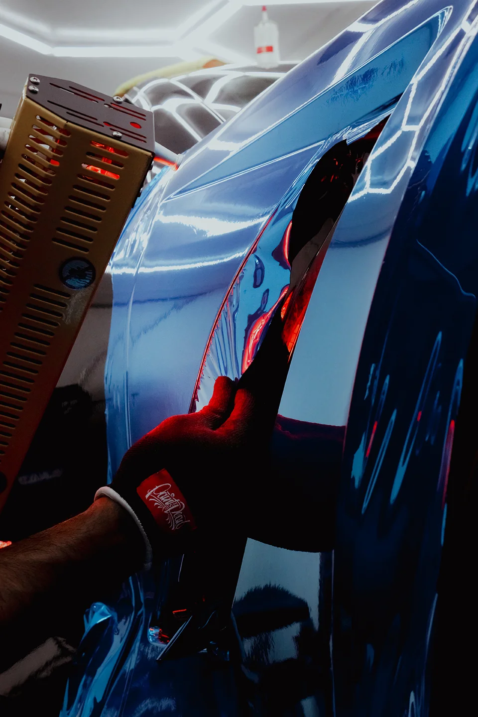 A technician applying heat during the installation of a blue chrome car wrap on a Chevrolet Corvette C7 at Allure Auto Spa