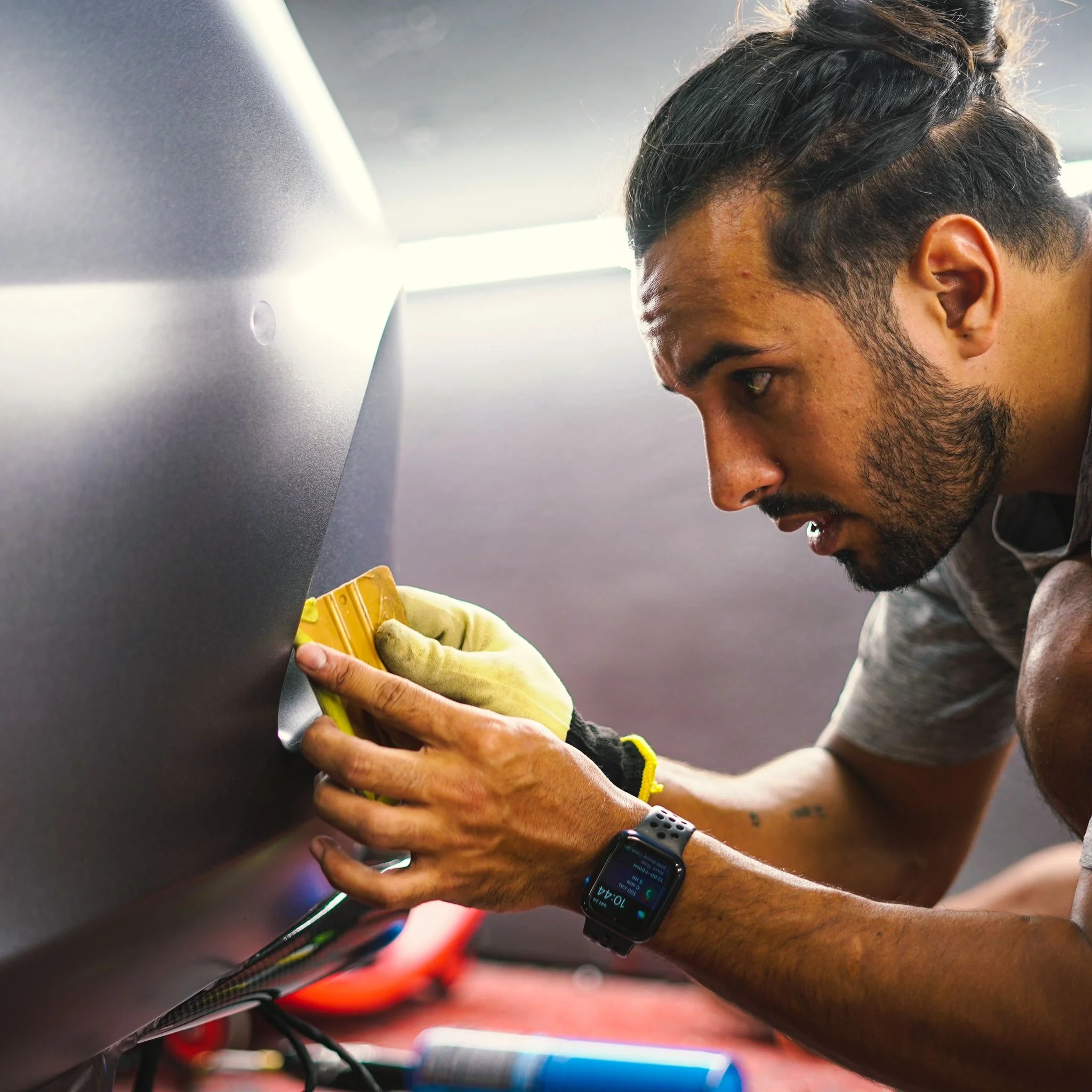 A skilled car wrap technician using a squeegee to smooth vinyl on a vehicle panel at Allure Auto Spa