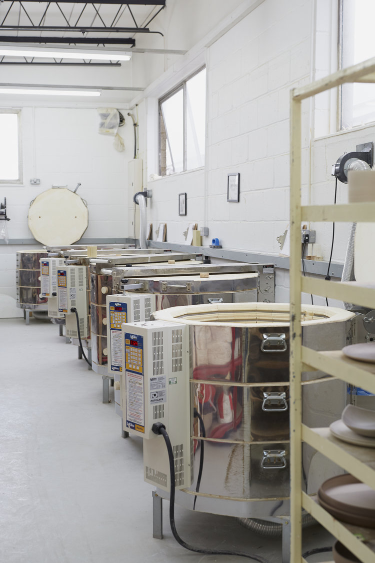 A row of electric kilns beside shelves of members' work at Turning Earth Leyton