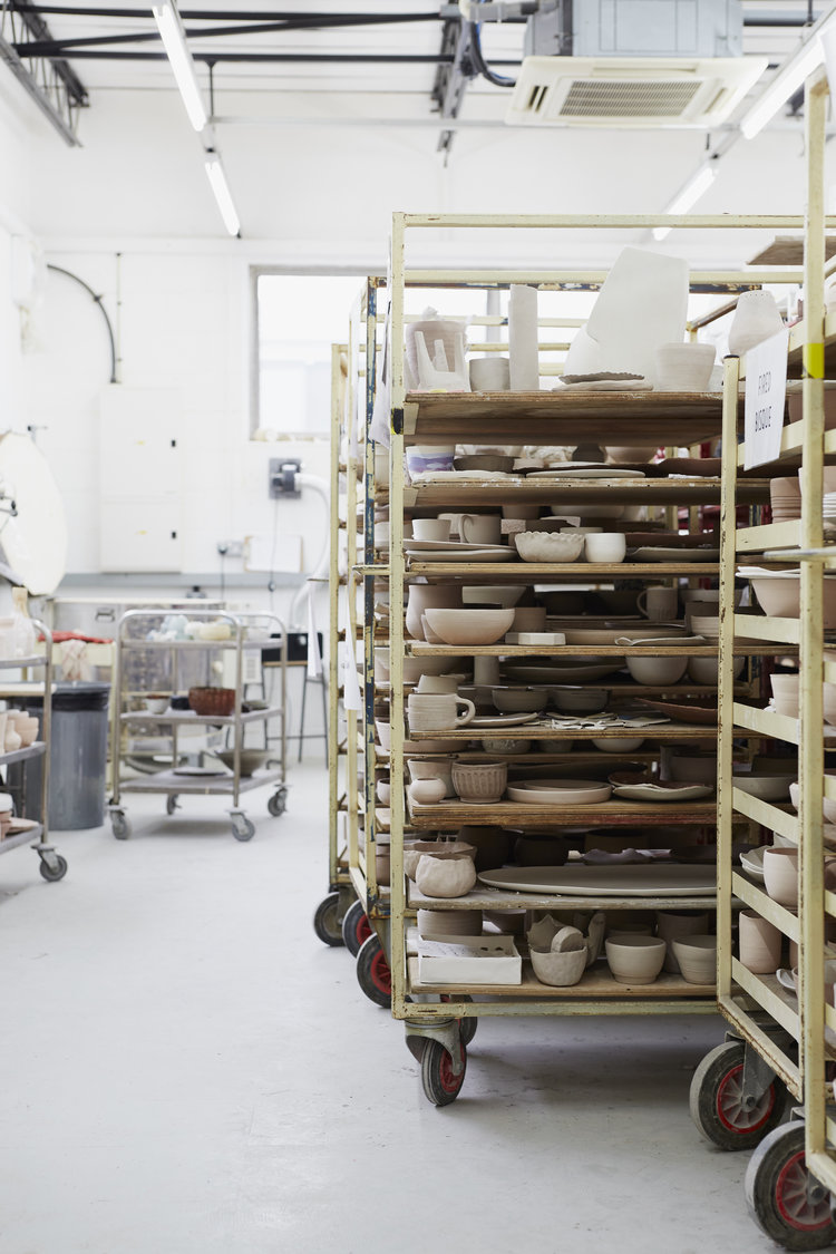 Racks on wheels loaded with members' unglazed pots at Turning Earth Leyton