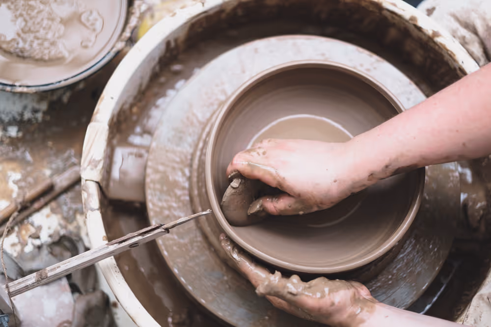 Three people shaping clay on pottery wheels in a ceramics class