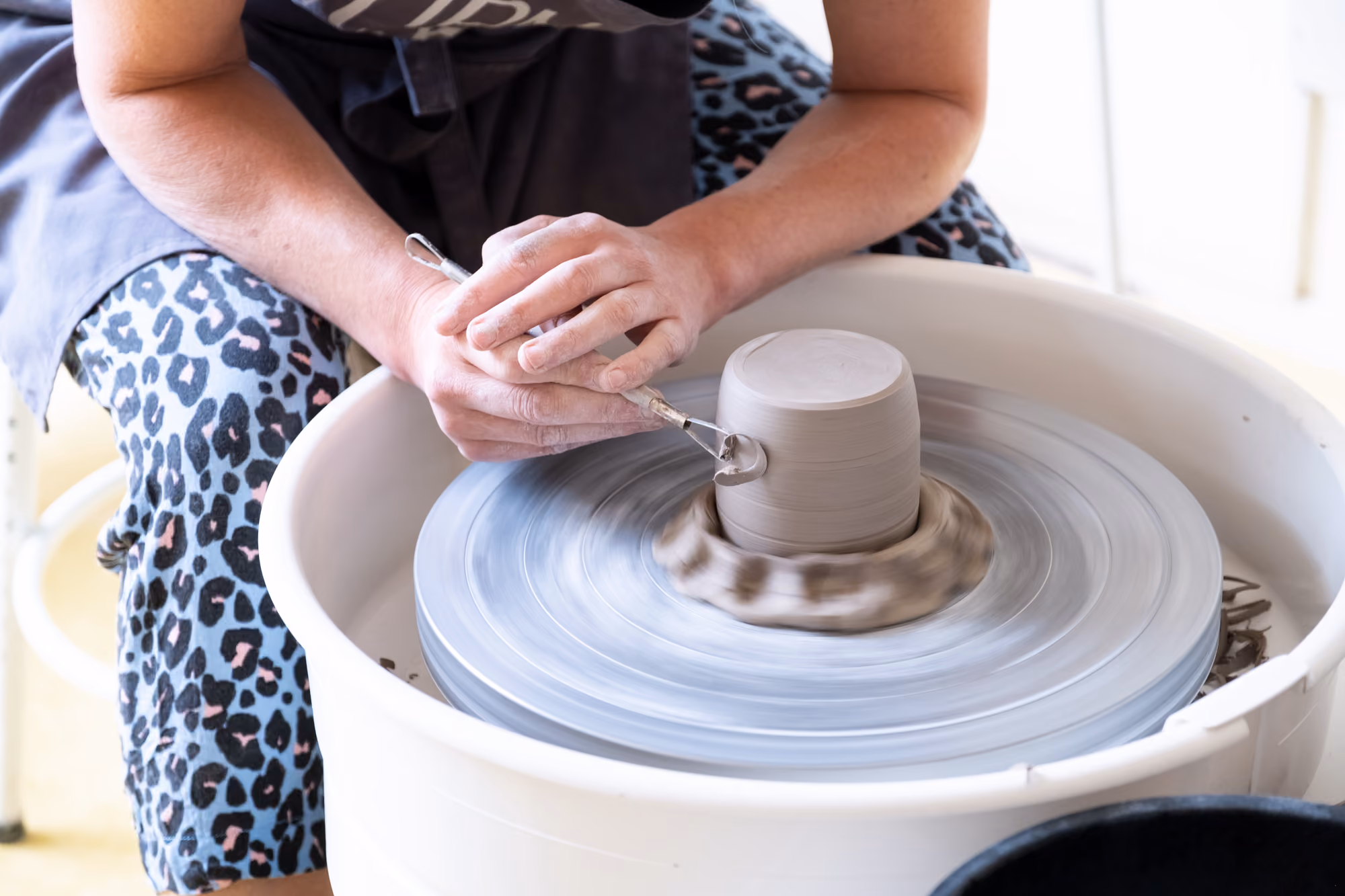 Hands sculpting a clay pot on a spinning pottery wheel.