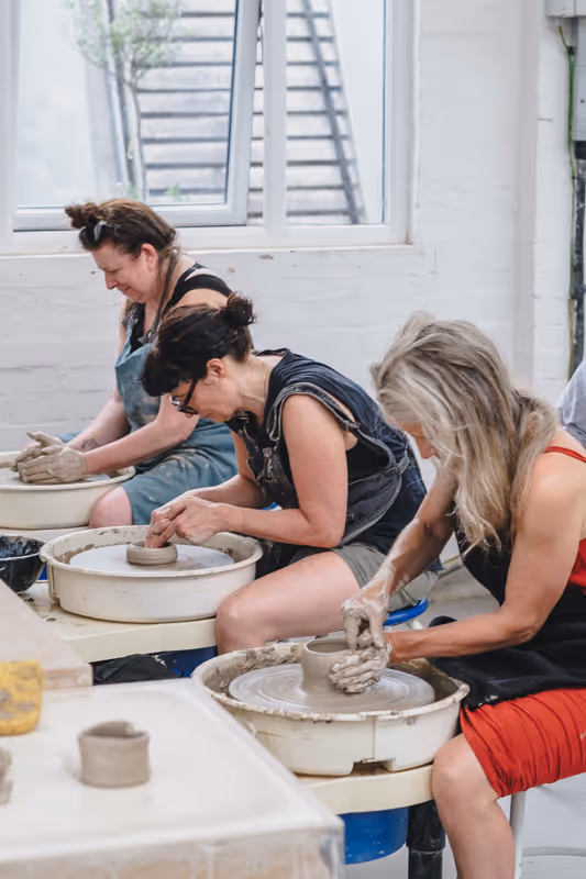 A young woman with braided hair shaping clay on a pottery wheel in a pottery class.