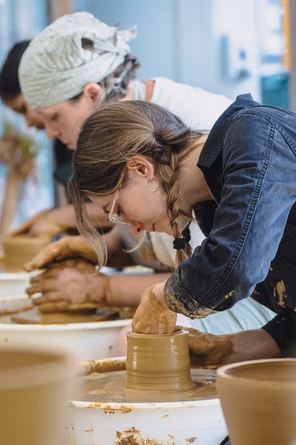 A young woman with braided hair shaping clay on a pottery wheel in a pottery class.