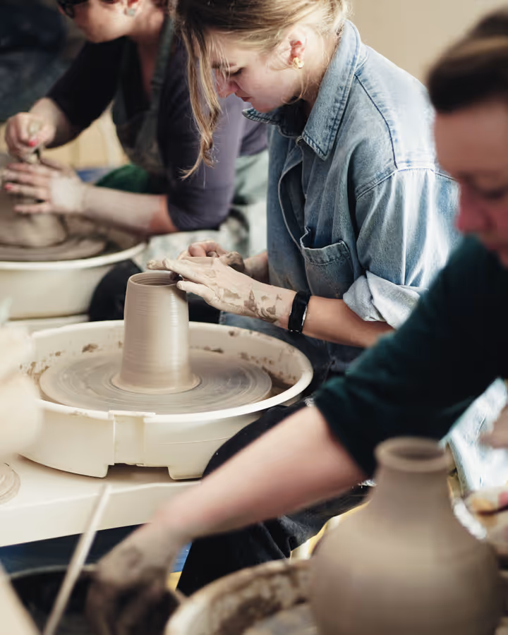 Three people shaping clay on pottery wheels in a ceramics class