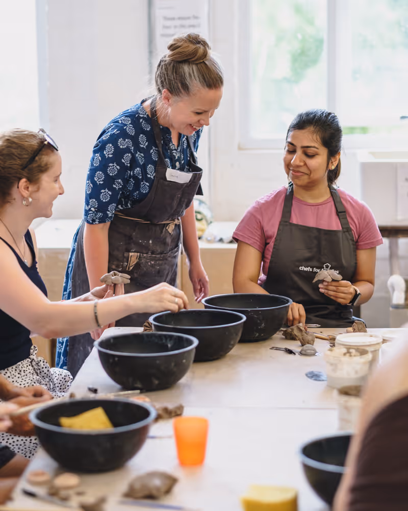 Three people shaping clay on pottery wheels in a ceramics class