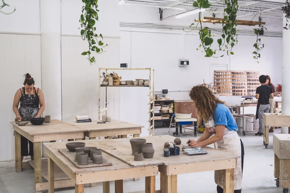 Students' finished glazed pottery laid out on a long table in a sunlit Turning Earth studio