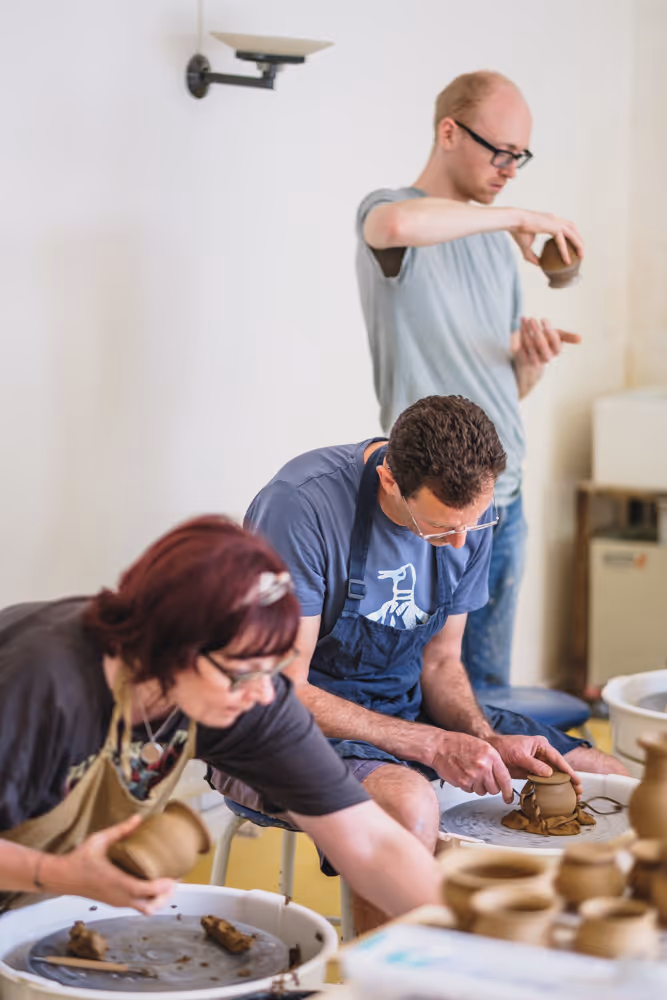 Three people shaping clay on pottery wheels in a ceramics class