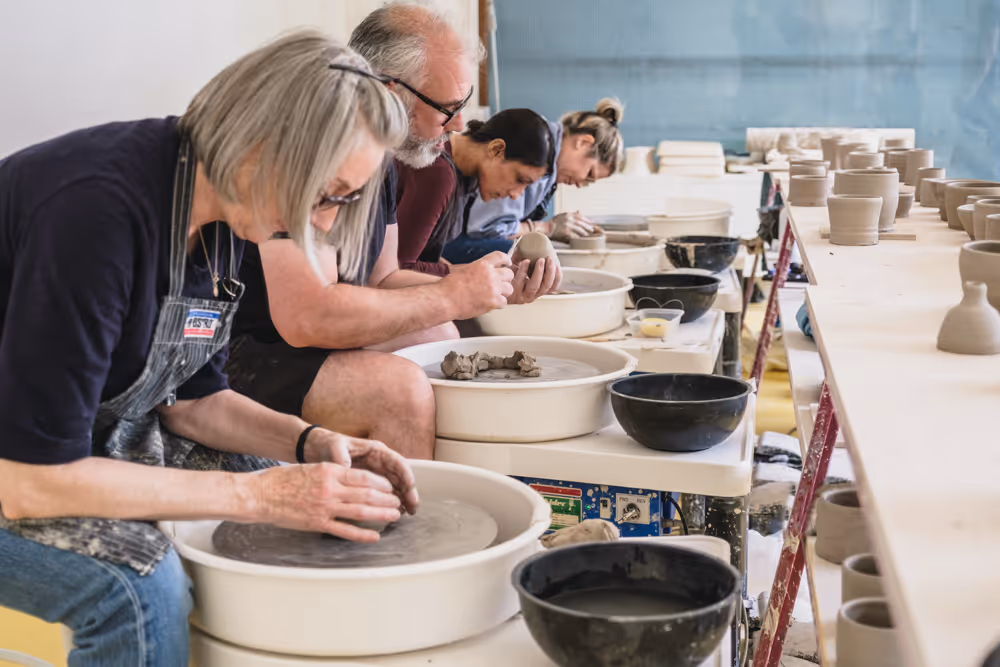 Three people shaping clay on pottery wheels