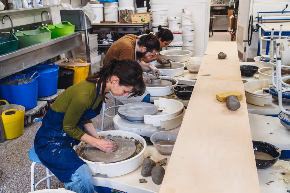 A young woman with braided hair shaping clay on a pottery wheel in a pottery class