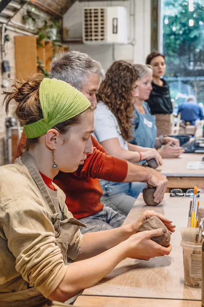 A young woman with braided hair shaping clay on a pottery wheel in a pottery class