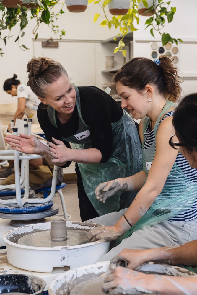 A young woman with braided hair shaping clay on a pottery wheel in a pottery class