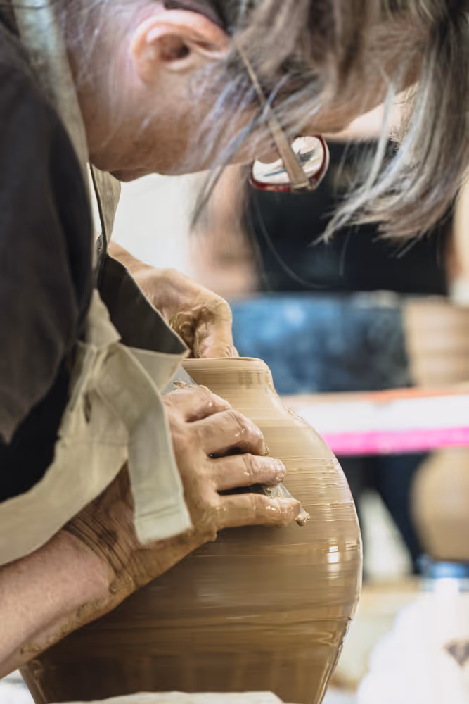 Students working on pottery around a table in a well-lit studio with large windows
