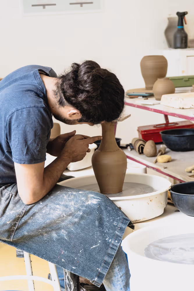 Students working on pottery around a table in a well-lit studio with large windows