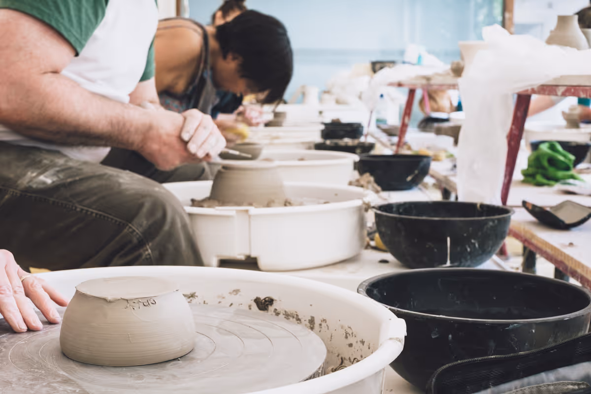Three people shaping clay on pottery wheels in a ceramics class