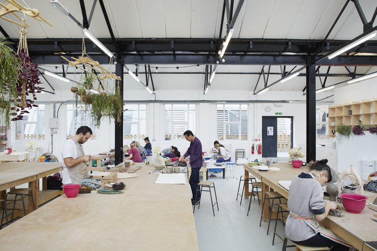 Makers working at long hand-building benches in Leyton's bright, high-ceilinged pottery studio