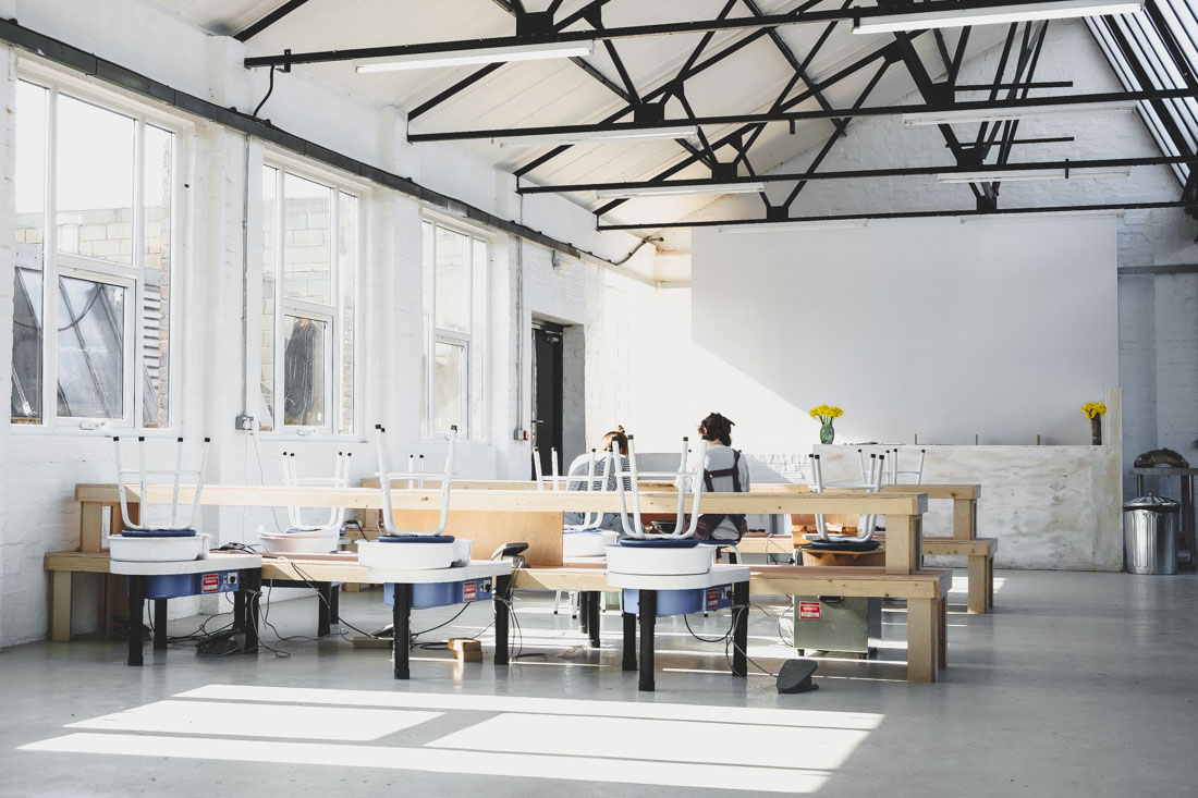 Pottery wheels lined up in the bright, white-painted main room at the Leyton studio, with daylight through tall windows