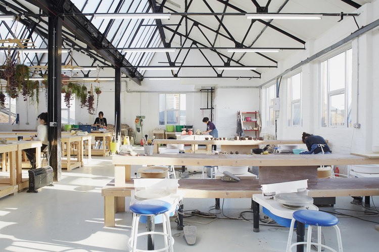 Potters at work on the wheels and benches in the daylit Leyton studio, with plants hanging from the roof