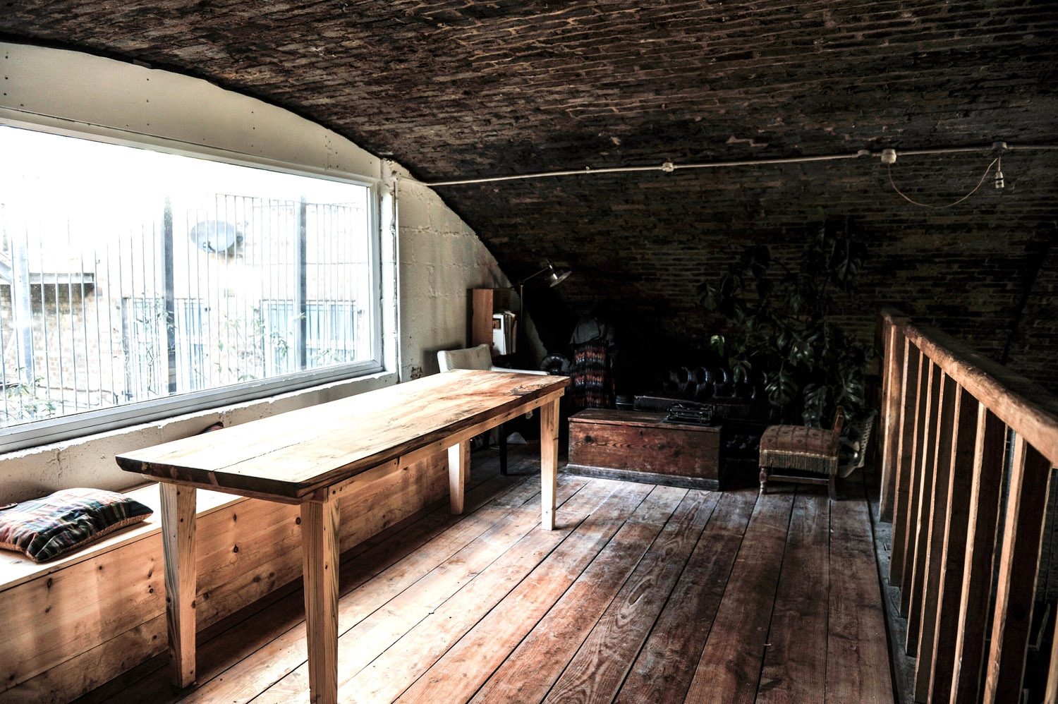 Mezzanine under the brick arch at the Hoxton studio, with a long wooden table by the window and a sofa